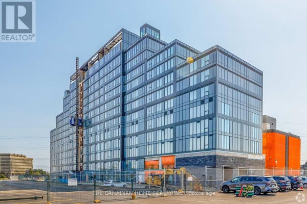 Construction view of a large glass commercial building with scaffolding and orange garage doors. - 227 - 600 Dixon Road, Toronto
