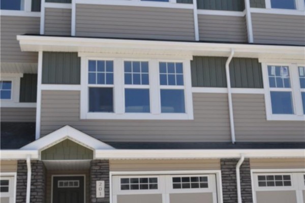 Exterior view of a townhouse with beige and green siding, white trim, and multiple windows. - 227 1220 Pringle Way, Saskatoon