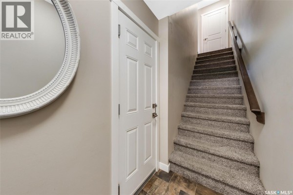 Interior view of a townhouse foyer with a white door, oval mirror, and carpeted stairs. - 227 1220 Pringle Way, Saskatoon