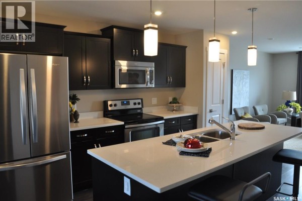 Kitchen with dark cabinets, stainless steel appliances, quartz countertops, and an island with stools. - 227 1220 Pringle Way, Saskatoon