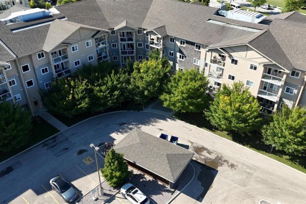 Aerial view showing building entrance, parking lot, and surrounding trees. - 227 230 Fairhaven Road, Winnipeg