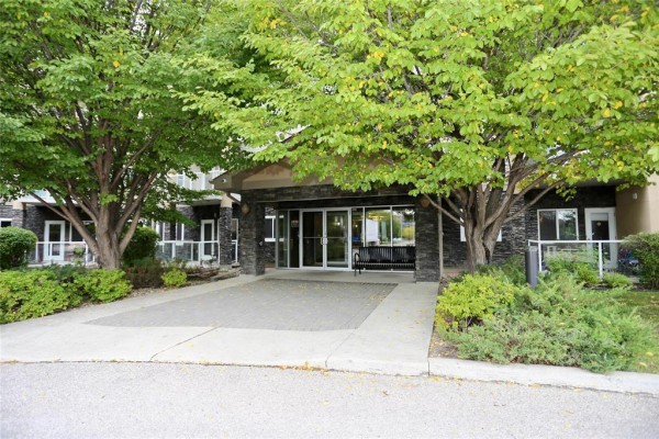 Building entrance with stone facade, glass doors, and covered walkway. - 227 230 Fairhaven Road, Winnipeg