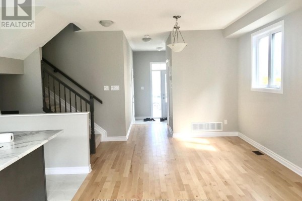 Open concept living area with light wood floors, neutral walls, and a staircase with black railings. - 227 Bandelier Way, Ottawa