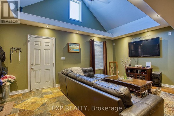 Living room with a sectional sofa, television, fireplace, and door, featuring stone and wood flooring. - 227 Beach Road, Hamilton