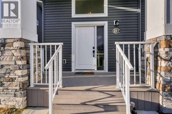 Close-up of the front door and porch with gray siding and stone details. - 227 Livingston Close, Red Deer