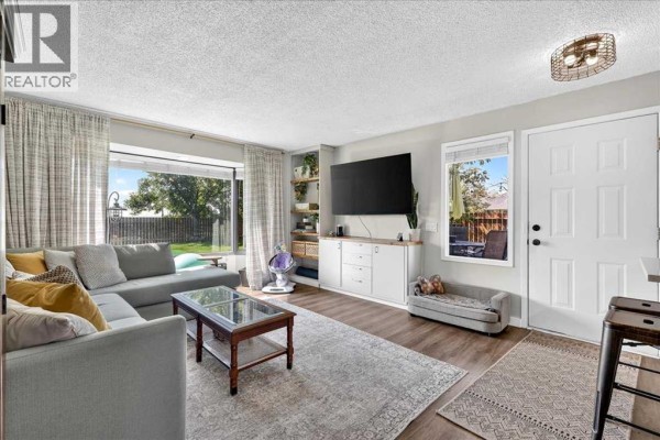 Living room with a large grey sectional sofa, coffee table, entertainment unit, and large window overlooking the backyard. - 227 Lynnwood Drive Se, Calgary