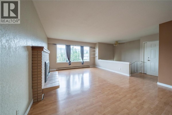 Living room with a white sofa, two armchairs, a coffee table, and a fireplace. - 2270 Greenfield Avenue, Kamloops