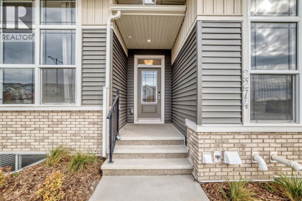 Close-up of the townhouse entrance with steps, a glass-paned door, and grey siding. - 2274 Bayview Drive Sw, Airdrie