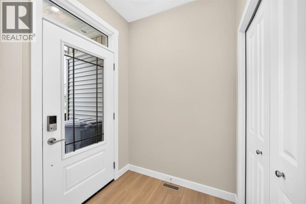 Interior entryway with a white door, beige walls, and light wood flooring. - 2274 Bayview Drive Sw, Airdrie