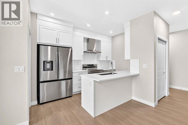 Modern white kitchen with stainless steel appliances, a kitchen island, and light wood floors. - 2274 Bayview Drive Sw, Airdrie