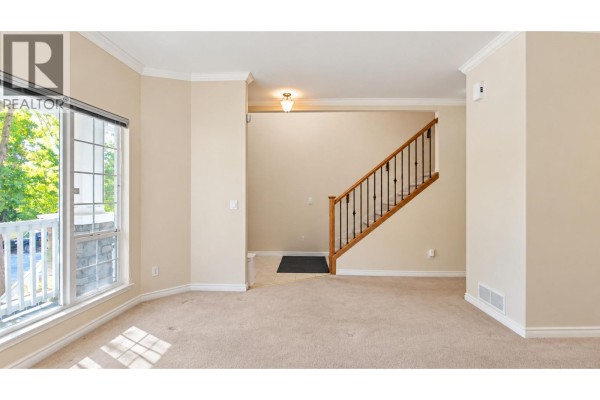 Living room with tan carpet, view of the staircase, and an entryway with tile flooring. - 22789 116 Avenue, Maple Ridge