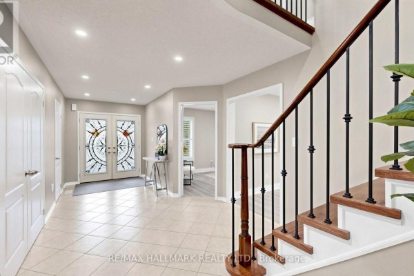 Spacious entryway with beige tile flooring, double glass doors, and a wooden staircase with black spindles. - 2279 Hackett Place, Oshawa