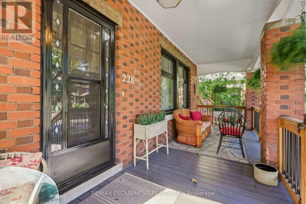 View of the porch with wicker furniture, a plant stand, and the front door. - 228 Sherman Avenue S, Hamilton