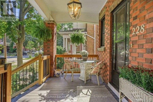 Porch detail showing a table and chairs, a hanging light fixture, and brick exterior. - 228 Sherman Avenue S, Hamilton