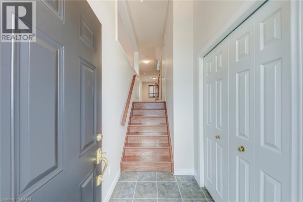 View from open doorway into a foyer with tiled floor and wooden stairs. - 2280 Baronwood Drive Unit# 18, Oakville
