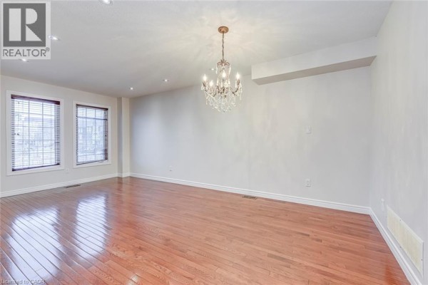 Living room with hardwood floors, white walls, two windows, and a chandelier. - 2280 Baronwood Drive Unit# 18, Oakville