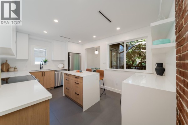 Modern kitchen with white counters, wood cabinets, stainless steel appliances, and an island with bar stools. - 2280 Blenheim Street, Vancouver
