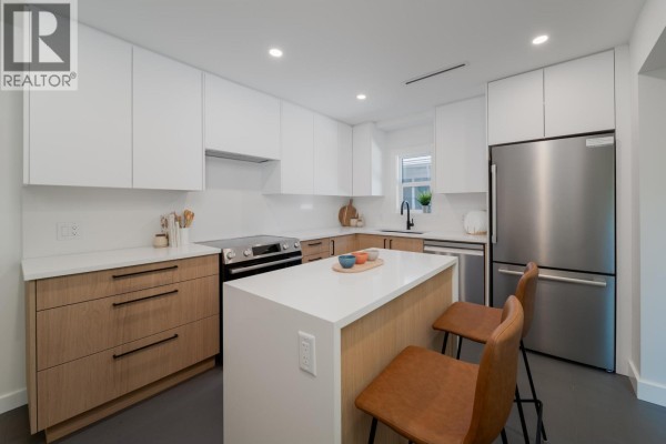 Kitchen with white cabinets, wood lower cabinets, stainless steel appliances, and a central island with bar stools. - 2280 Blenheim Street, Vancouver