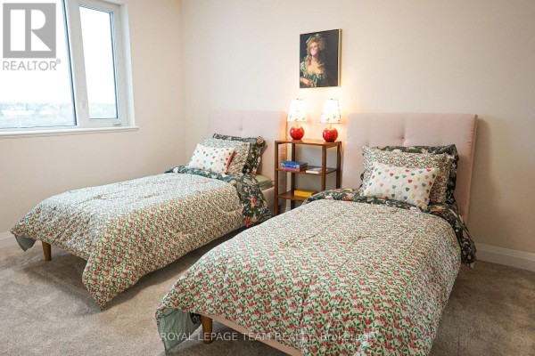 Bedroom with two twin beds, patterned bedding, and a small wooden shelf with decorative lamps. - 229 - 1050 Canadian Shield Avenue, Ottawa
