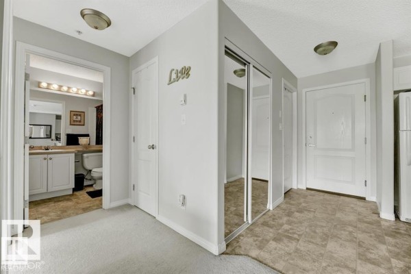 Apartment hallway with light grey walls, white doors, mirrored closet doors, and access to a bathroom. - #229 1520 Hammond Gate Nw, Edmonton