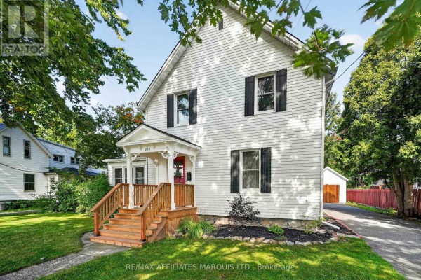 Close-up of the white house exterior showing a red front door and wooden porch. - 229 4th Street E, Cornwall