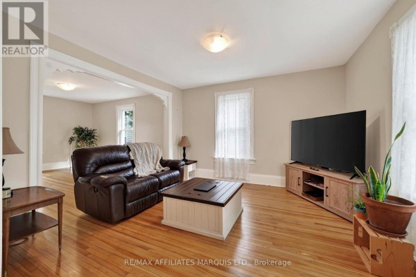 Living room with hardwood floors, a large TV, a leather recliner, and an arched doorway. - 229 4th Street E, Cornwall