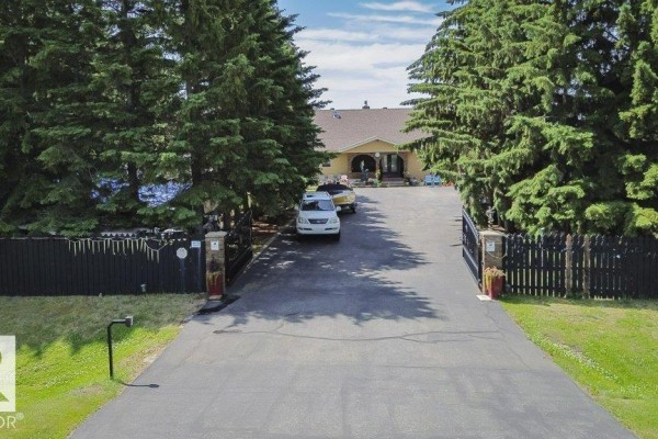 Exterior view of a large beige house with multiple windows and a wooden deck, set in a cleared grassy field. - #229 53310 Rge Road 221, Rural Strathcona County