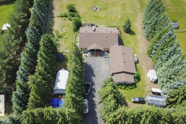 Aerial view of a wide, cleared grassy field with scattered trees and a residential building in the distance. - #229 53310 Rge Road 221, Rural Strathcona County