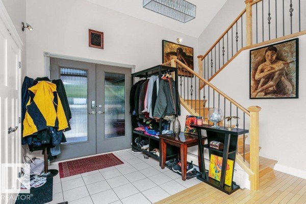 Rear view of a beige house featuring a spacious wooden deck with outdoor furniture and surrounding evergreen trees. - #229 53310 Rge Road 221, Rural Strathcona County