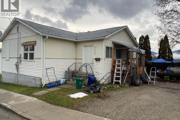 Front view of a white sided house with covered porch, yard tools, and mountains. - 229 9th  S Avenue, Creston