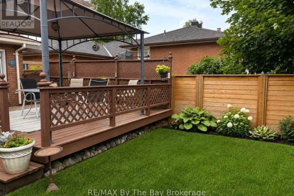 Wooden deck with a gazebo, table, and chairs overlooking a green lawn and wooden fence. - 229 Datas Drive E, Clearview