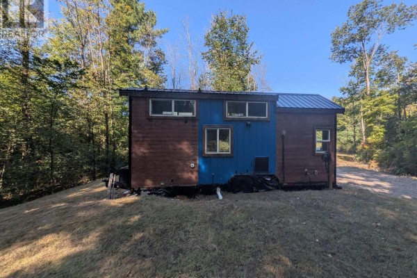 Side view of a mobile home with brown and blue siding, showing multiple windows and exterior elements, surrounded by grass. - 229 Norris Road, Tay Valley