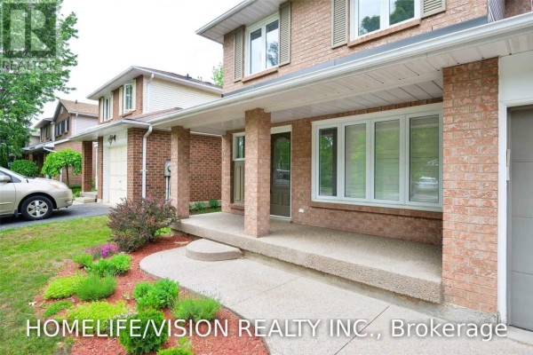 Close-up of the covered front porch with brick pillars, concrete floor, and landscaping. - 229 Village Wood Road, Oakville