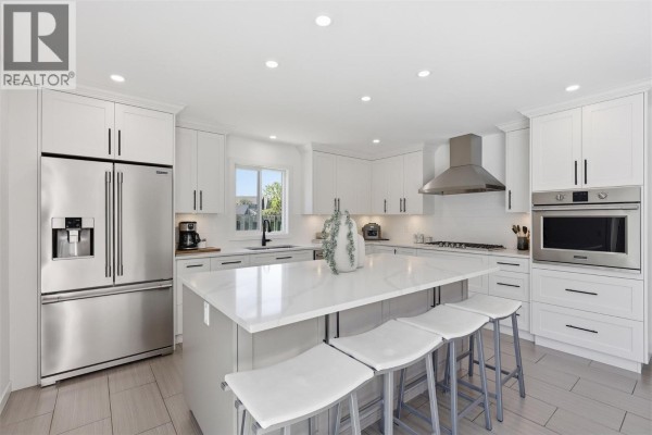 Modern kitchen with white cabinets, an island with bar stools, and sliding doors to a pool area. - 2298 Balfour Court, Kamloops