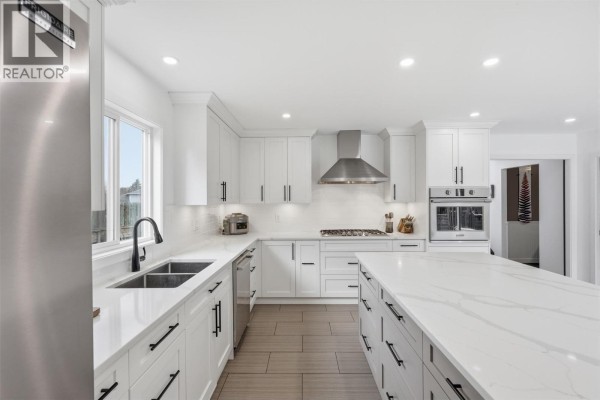 Bright kitchen with white cabinets, stainless steel appliances, a large island, and a sink overlooking the backyard. - 2298 Balfour Court, Kamloops