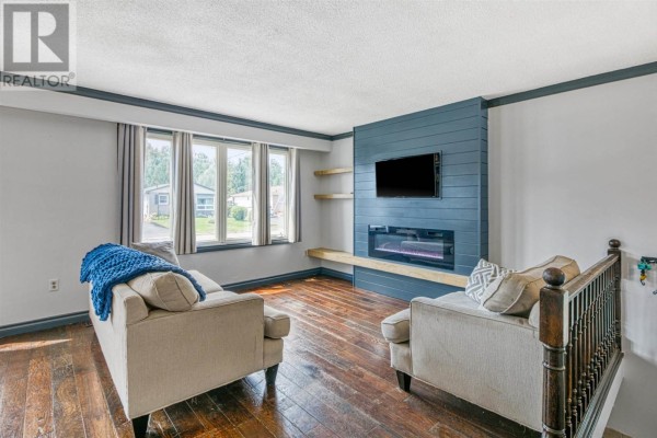 Living room with two sofas, a fireplace with a mounted television, and wood flooring. - 22a Ottawa Ave, Elliot Lake