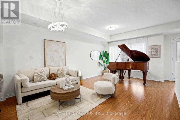 Living room with beige sofa, round coffee table, and a grand piano beside a window. - 23 - 1 Eaton Park Lane E, Toronto