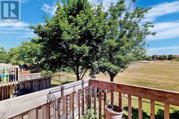 View from a wooden balcony overlooking a grassy field and trees under a blue sky. - 23 - 1588 South Parade Court, Mississauga