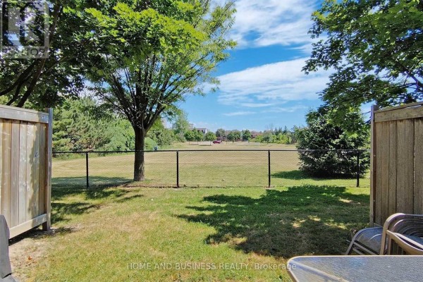 View of a green field and trees through a wooden fence opening with patio furniture. - 23 - 1588 South Parade Court, Mississauga