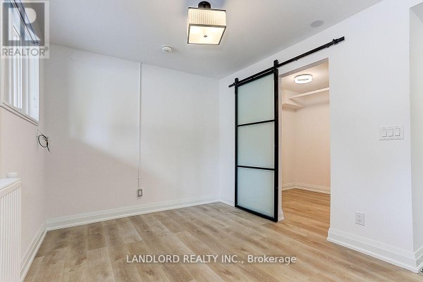 Empty room with light wood flooring and a frosted glass barn door leading to another room. - 23 - 2520 Bloor Street W, Toronto