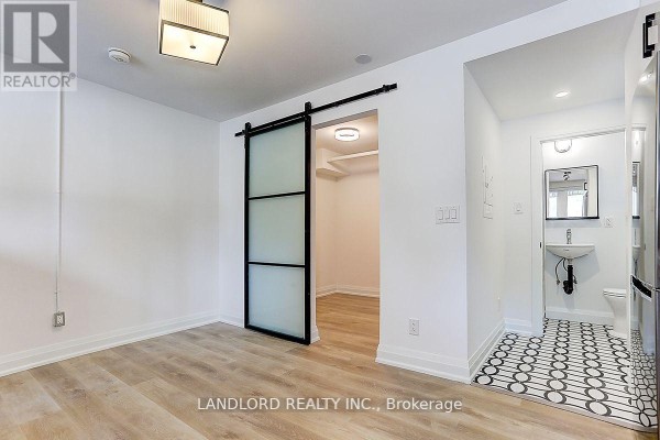 Room with frosted barn door, view into a bathroom with a sink and toilet, black and white tiled floor. - 23 - 2520 Bloor Street W, Toronto