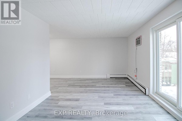 Empty living space with light gray wood-look flooring and a large window on the right. - 23 - 6287 O'neil Street, Niagara Falls