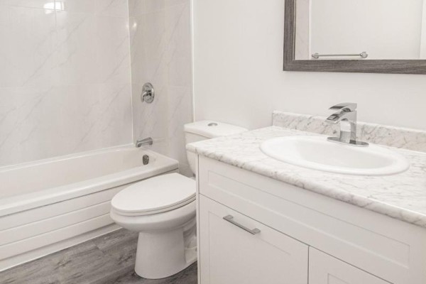 Clean bathroom with a white tub, toilet, vanity, marble-look countertop, and a mirror. - 23 - 6287 O'neil Street, Niagara Falls