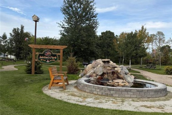 A wooden archway with "Adeline's Park" sign stands near a rock waterfall pond and a wooden bench. - 23 1st Avenue S, Ashern