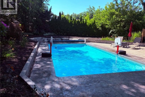 Backyard with an in-ground swimming pool, concrete patio, lounge chairs, and mature trees. - 23 Bentley Place, Hamilton