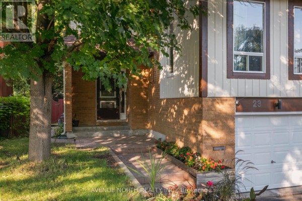 Close-up of the front entrance showing a brick facade, paved walkway, and foliage with flowers. - 23 Bluegrass Drive, Ottawa