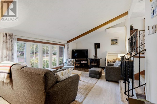 Living room with large windows, sectional sofa, two armchairs, a wood stove, and a wood beam ceiling. - 23 Country Club Pl, Sault Ste  Marie
