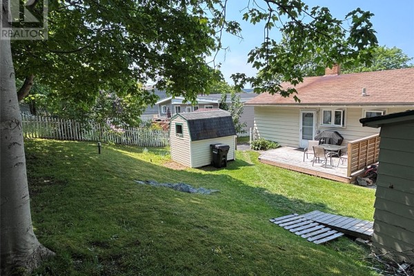 Backyard view with a wooden deck, shed, and green lawn surrounded by trees. - 23 Diana Road, St  John S