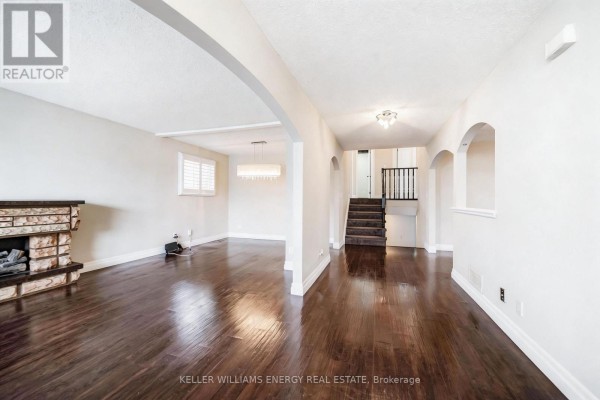 Living room with dark hardwood floors, a stone fireplace, and arched openings to other rooms. - 23 Downham Drive, Clarington