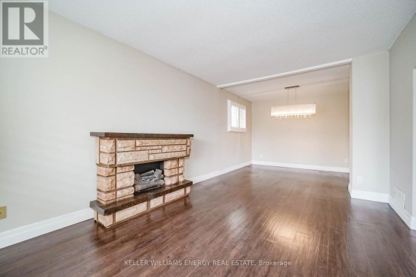 Living room featuring a stone fireplace, dark hardwood floors, and an opening to the dining area. - 23 Downham Drive, Clarington